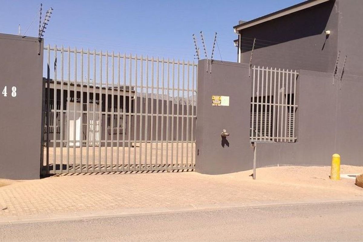 Secure industrial property entrance featuring a gated driveway, perimeter wall with electric fencing, and paved access area.