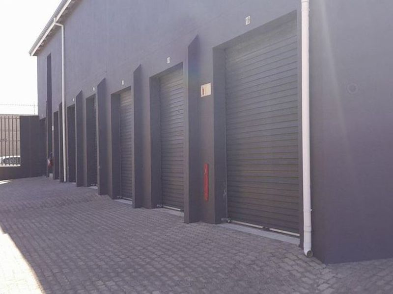 Exterior view of an industrial complex featuring multiple roller shutter doors, paved driveway access, and secure perimeter fencing.