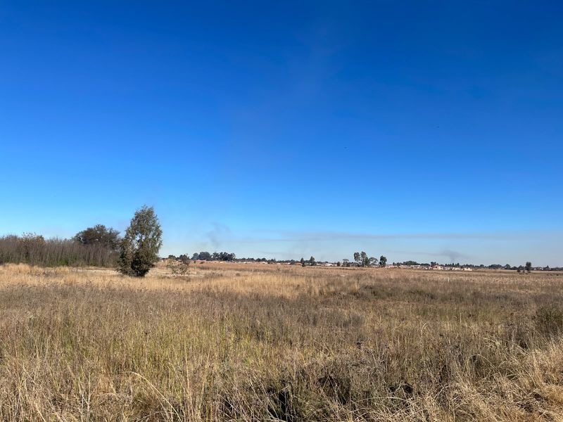 A wide-angle view of a vacant commercial land plot featuring natural grass and surrounding landscape.