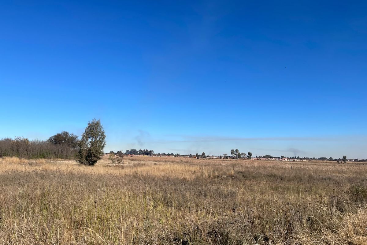 A wide-angle view of a vacant commercial land plot featuring natural grass and surrounding landscape.