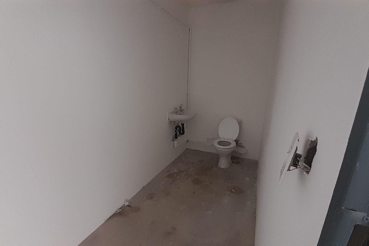 A basic, unfinished bathroom space featuring a toilet, wall-mounted basin, and exposed plumbing, requiring significant renovation and finishing work.