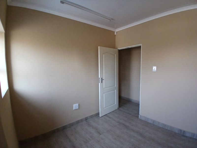 A clean, empty bedroom featuring neutral wall paint, modern laminate flooring, and a simple internal door leading to an adjacent space.