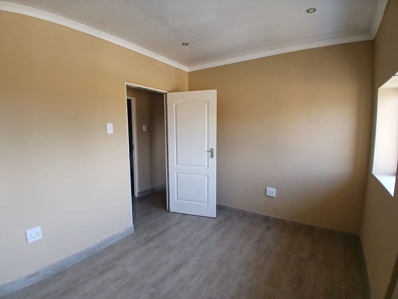 A clean, empty bedroom featuring neutral wall paint, modern laminate flooring, and recessed ceiling lighting.