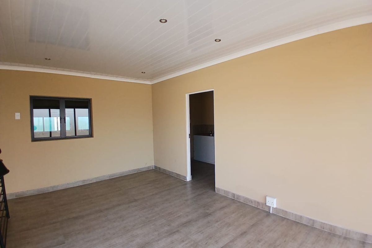 A clean, empty living area featuring modern laminate flooring, recessed ceiling lighting, and neutral wall tones, providing a versatile space for various industrial office uses.