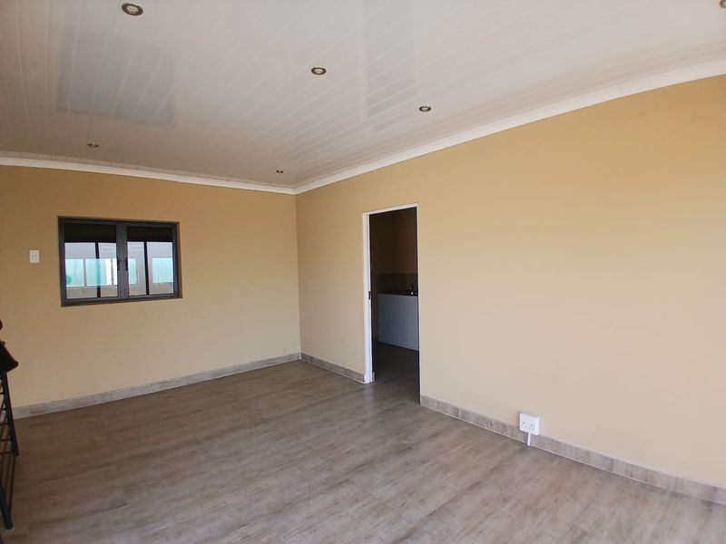 A clean, empty living area featuring modern laminate flooring, recessed ceiling lighting, and neutral wall tones, providing a versatile space for various industrial office uses.