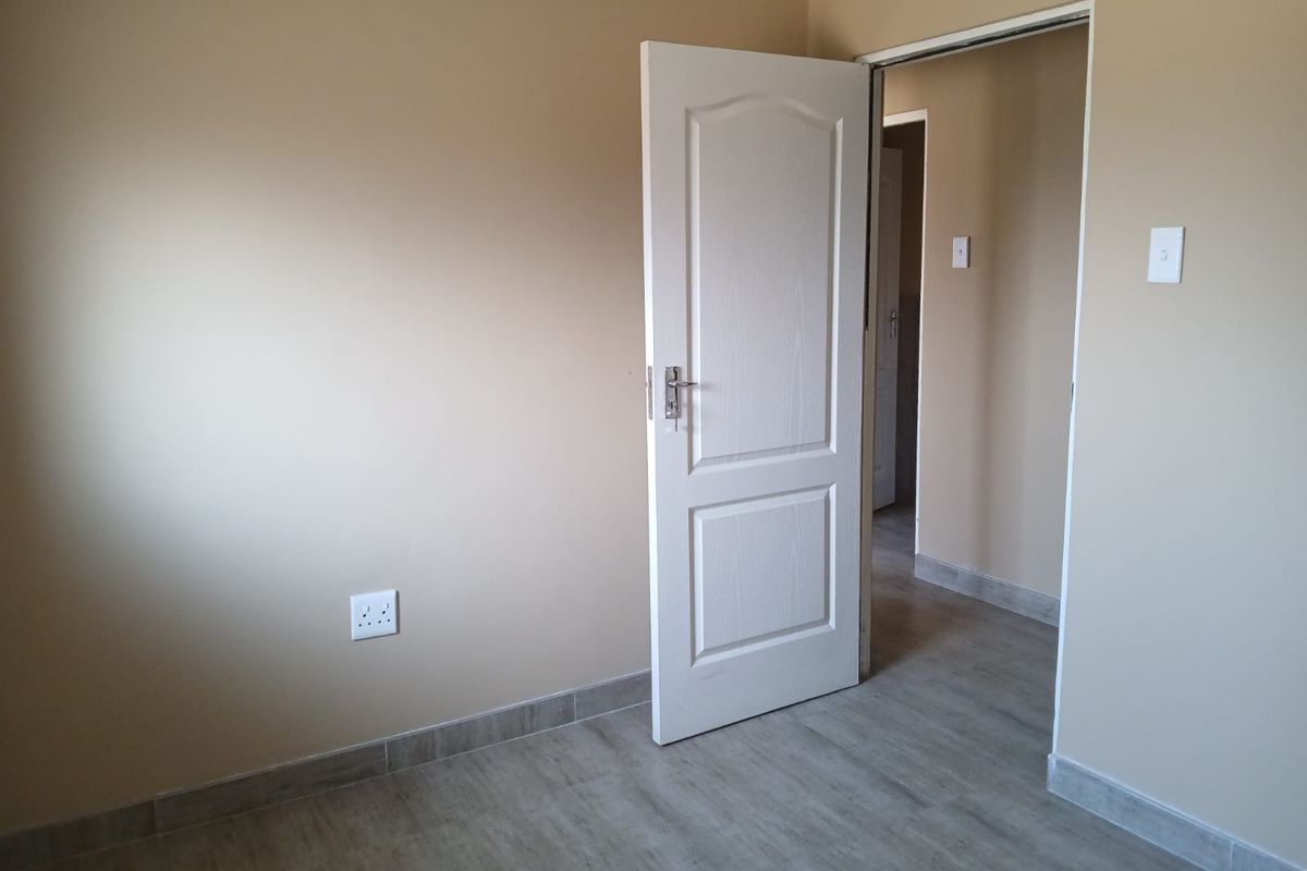 A clean, empty bedroom featuring neutral wall paint, modern tiled flooring, and a white internal door leading to a hallway.