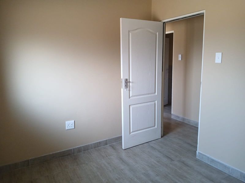 A clean, empty bedroom featuring neutral wall paint, modern tiled flooring, and a white internal door leading to a hallway.