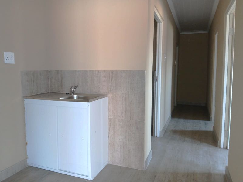 A functional scullery or utility area featuring a stainless steel sink, built-in vanity cabinet, and tiled splashback, situated adjacent to a hallway.
