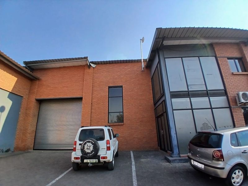 Industrial property exterior featuring a brick facade, large roller shutter door, and a multi-level glass office section with dedicated parking.