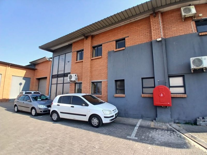 Exterior view of an industrial building featuring a brick and painted facade, metal roofing, and dedicated paved parking space with fire safety equipment.