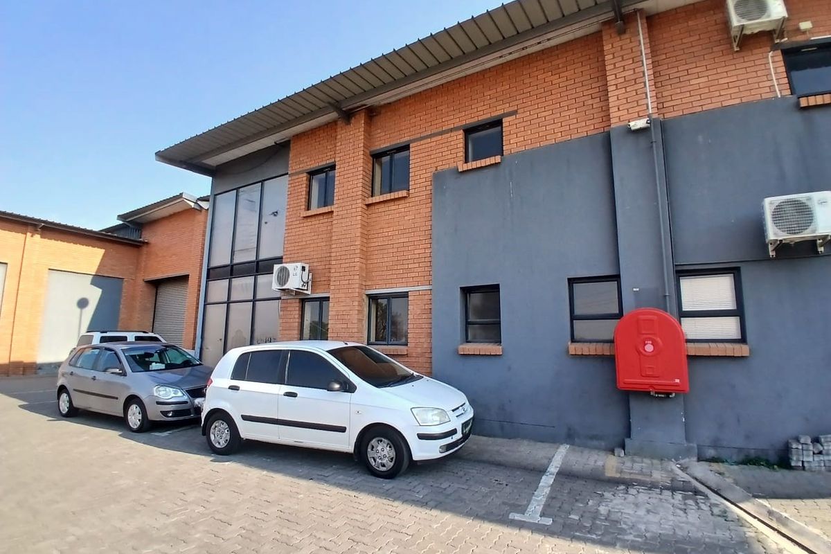 Exterior view of an industrial building featuring a brick and painted facade, metal roofing, and dedicated paved parking space with fire safety equipment.