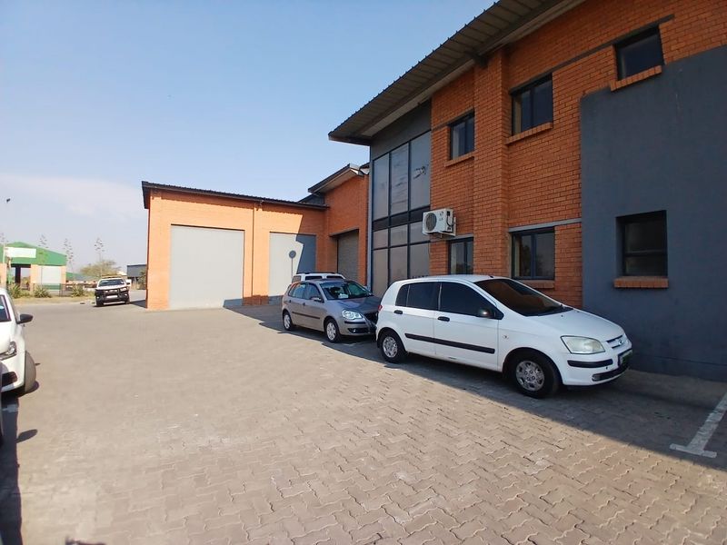 Exterior view of an industrial property featuring a brick facade, paved driveway, and multiple roller shutter doors for access.