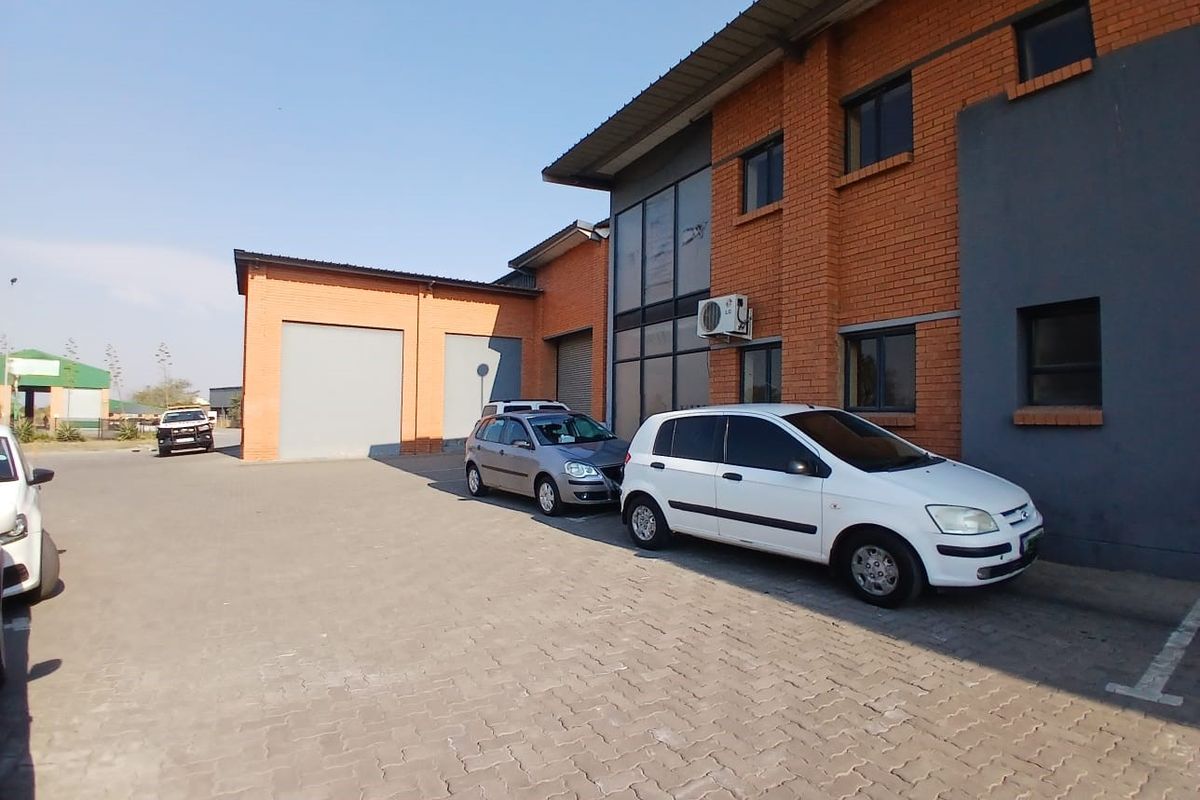 Exterior view of an industrial property featuring a brick facade, paved driveway, and multiple roller shutter doors for access.