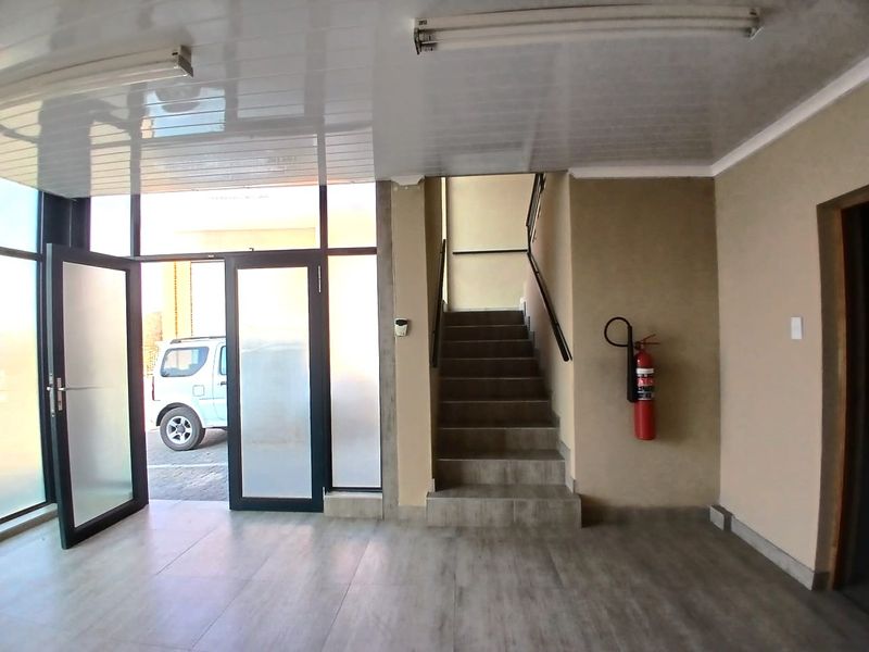 A clean and functional industrial entrance area featuring tiled flooring, a staircase leading to the upper level, and a wall-mounted fire extinguisher.