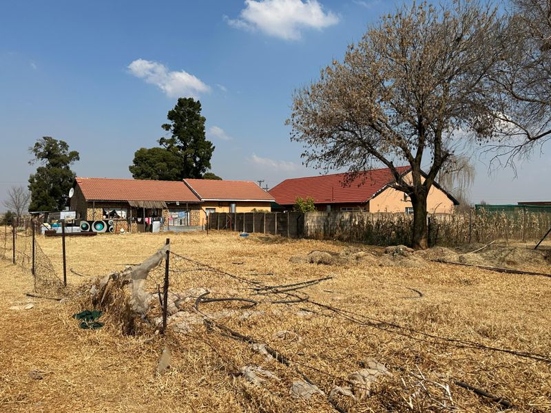 Rear view of the small holding property featuring multiple structures, a concrete boundary wall, and extensive open land with dry vegetation.