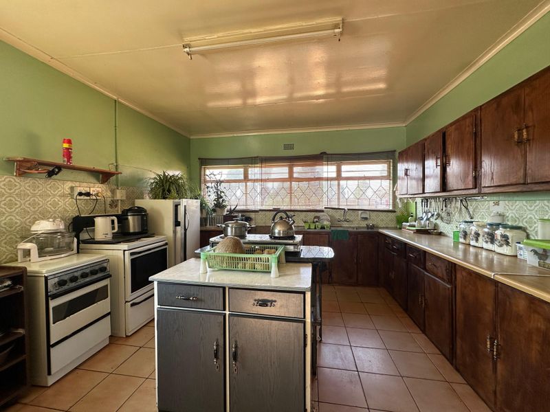 A spacious, dated kitchen featuring wooden cabinetry, a central island, tiled flooring, and a tiled backsplash, offering significant potential for modernization.