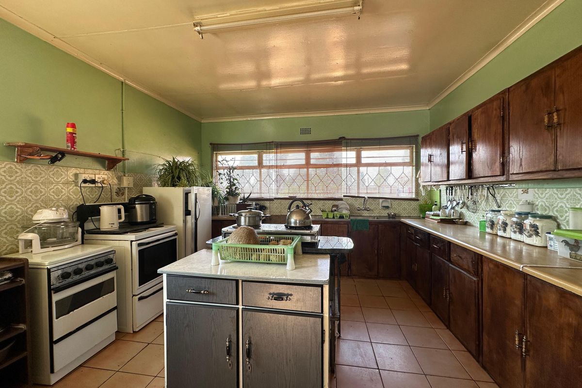 A spacious, dated kitchen featuring wooden cabinetry, a central island, tiled flooring, and a tiled backsplash, offering significant potential for modernization.