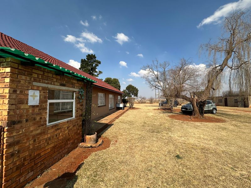 Rear view of a face-brick small holding dwelling featuring a corrugated roof and a covered patio area overlooking a large garden.