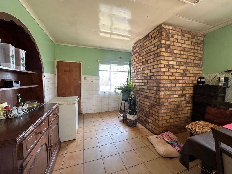 A dated kitchen area featuring an exposed brick chimney breast, ceramic tiled flooring, and tiled splashbacks, offering potential for a modern renovation.