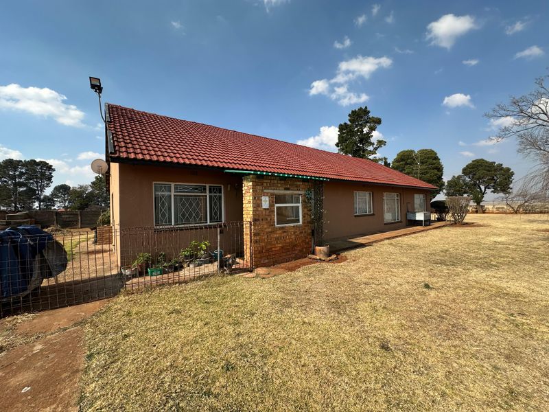 A single-story small holding residence featuring a tiled roof, brick accents, and security bars, set on a large, open grassed plot.