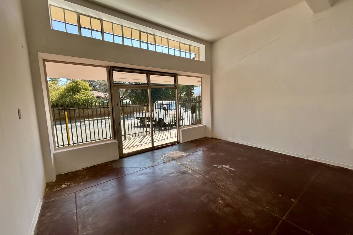 An empty retail space featuring large display windows, a sliding glass entrance door, and worn concrete flooring, offering a blank canvas for commercial use.