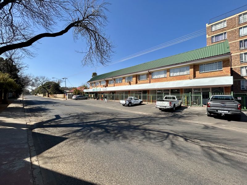 Street-level view of a multi-unit retail property featuring a brick facade, green metal roof, and dedicated off-street parking.