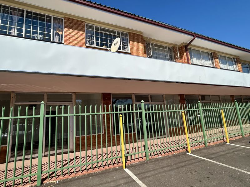 Front exterior view of a retail property featuring a brick facade, large glass storefront windows, and a secure metal fenced parking area.