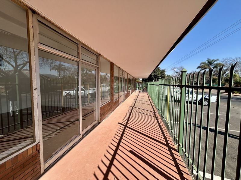 Front exterior view of a retail property featuring a covered walkway, large glass storefront windows, and secure metal perimeter fencing.
