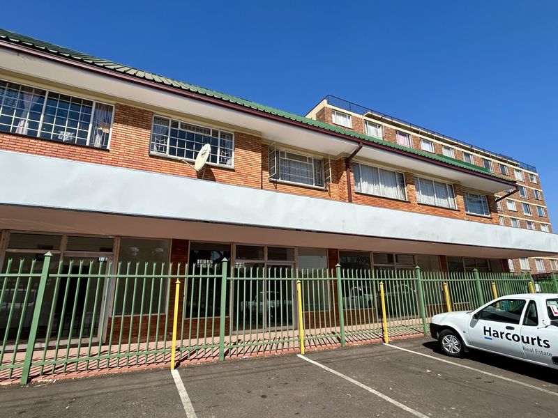 Front exterior view of a multi-story retail building featuring brick facade, security fencing, and dedicated paved parking area.