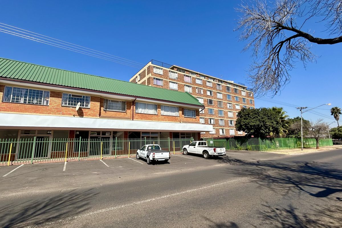 Front exterior view of a multi-story retail and residential building featuring a brick facade, green metal roof, and secure street-level parking.