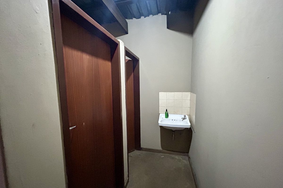 A functional bathroom area featuring a wall-mounted basin with tiled splashback and two timber doors leading to private stalls.