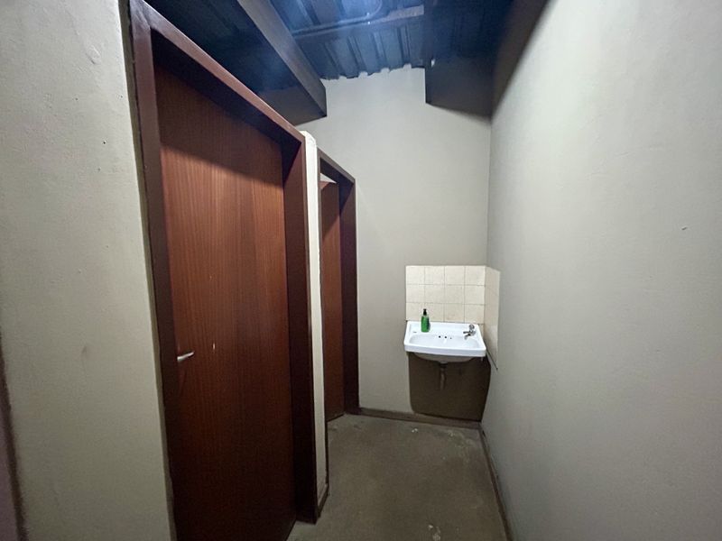 A functional bathroom area featuring a wall-mounted basin with tiled splashback and two timber doors leading to private stalls.