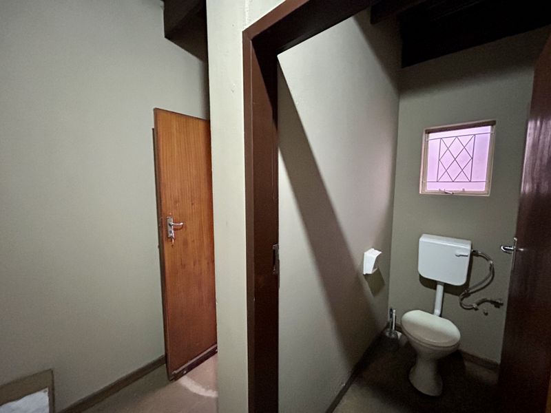 A functional, compact bathroom featuring a standard toilet, timber door, and a small window with security bars.