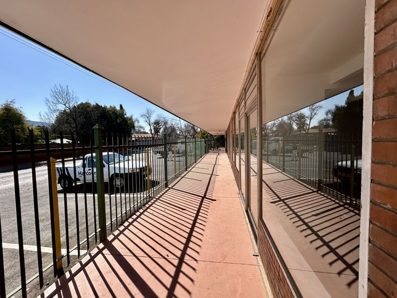 Exterior view of a retail storefront featuring a covered walkway, large glass display windows, and metal security fencing.