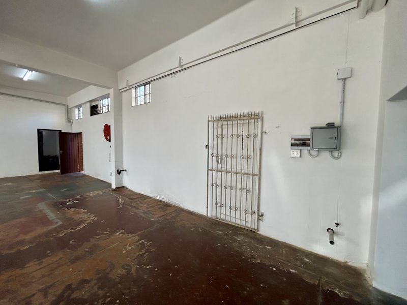 An empty utility or industrial space featuring exposed electrical conduits, a security gate, and worn concrete flooring, suitable for various commercial or storage uses.