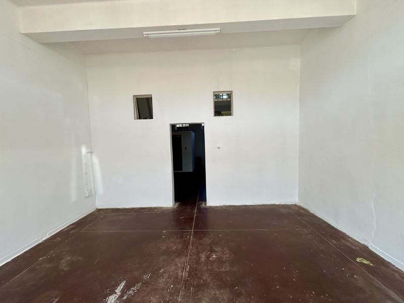 An empty, utilitarian retail space featuring white walls, a durable floor finish, and basic overhead lighting, suitable for various commercial or storage uses.