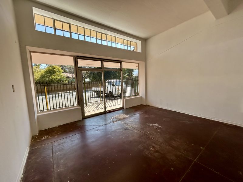 An empty retail space featuring large display windows, a sliding glass entrance door, and worn concrete flooring, offering a blank canvas for commercial use.