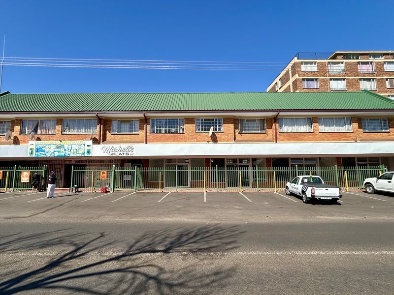 Front elevation of a multi-level retail and residential building featuring brick construction, a green metal roof, and secure ground-level parking.