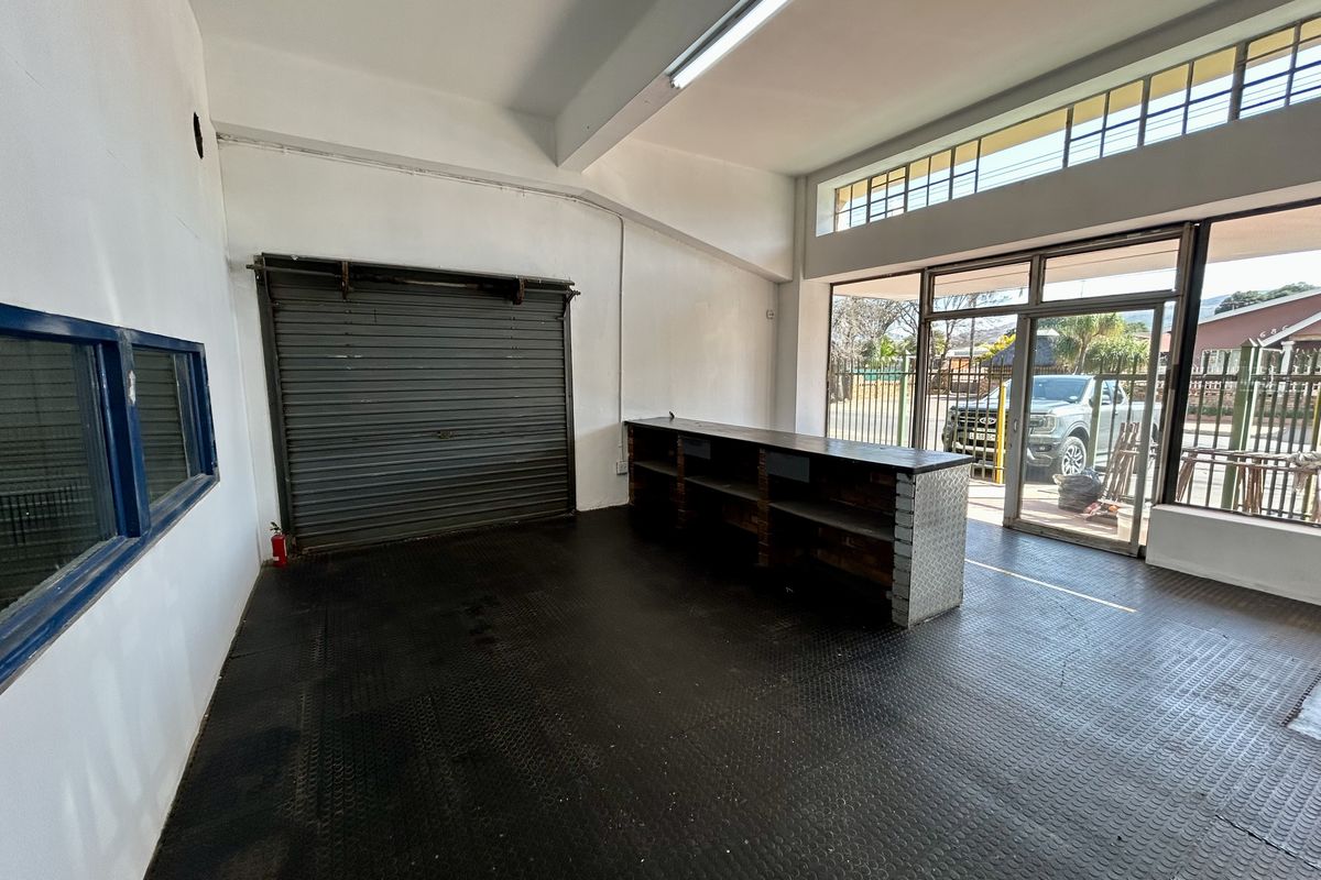 Open-plan retail or utility space featuring a built-in service counter, roller shutter door, durable rubberized flooring, and large windows providing natural light.