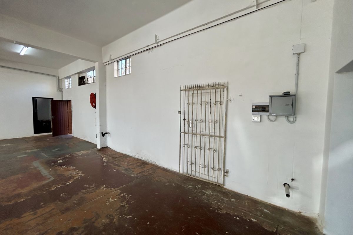 An empty utility or industrial space featuring exposed electrical conduits, a security gate, and worn concrete flooring, suitable for various commercial or storage uses.