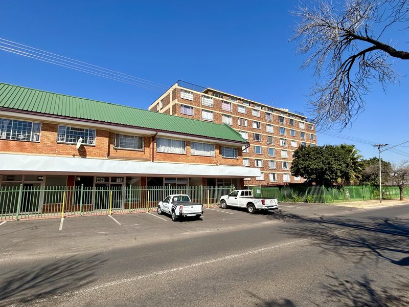 Front exterior view of a multi-story retail and residential building featuring a brick facade, green metal roof, and secure street-level parking.
