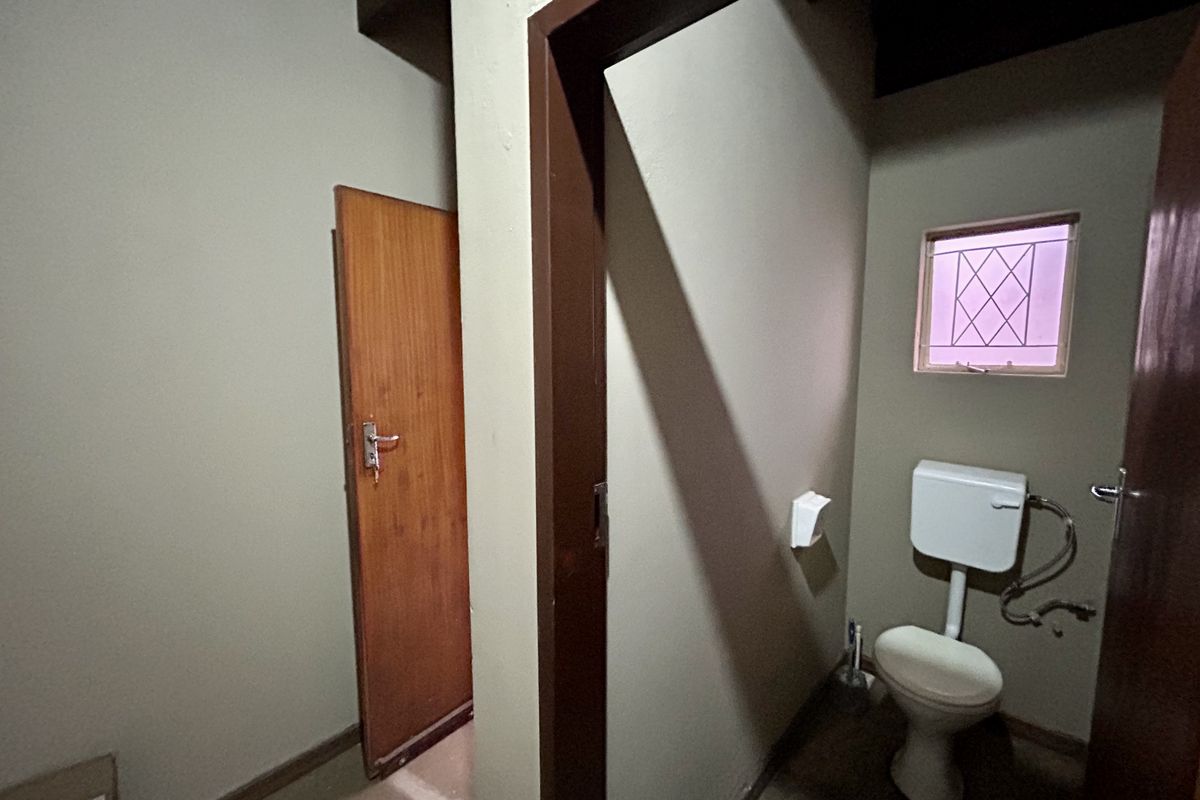A functional, compact bathroom featuring a standard toilet, timber door, and a small window with security bars.