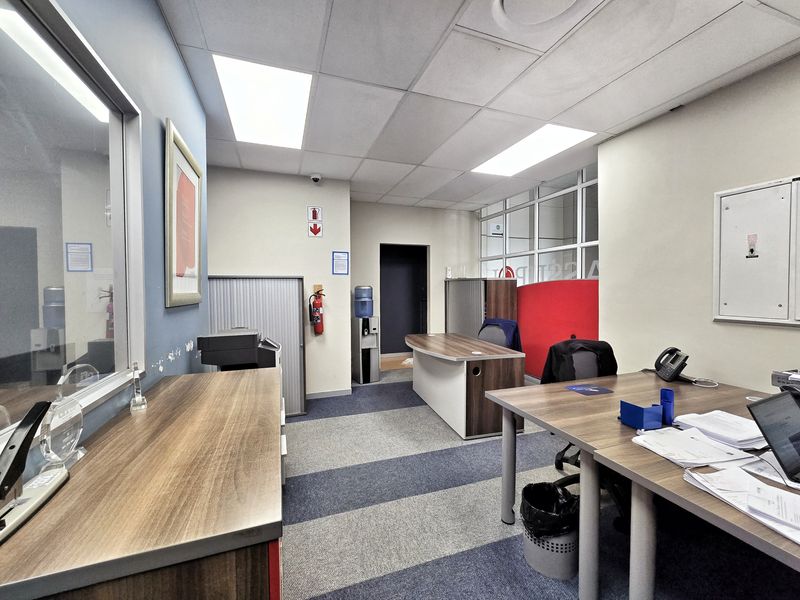 A functional office space featuring carpeted flooring, suspended ceiling with recessed lighting, and an internal glass partition wall.