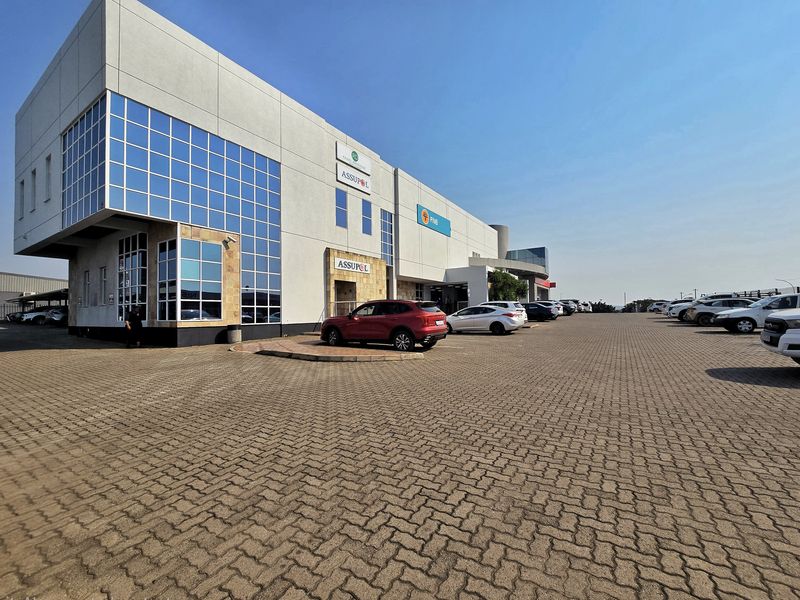 Modern commercial office building featuring a glass facade, stone cladding, and an extensive paved parking area for tenants and visitors.