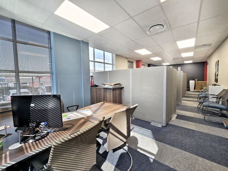 Open-plan office space featuring modular partition walls, suspended ceilings with recessed lighting, and large windows with venetian blinds.