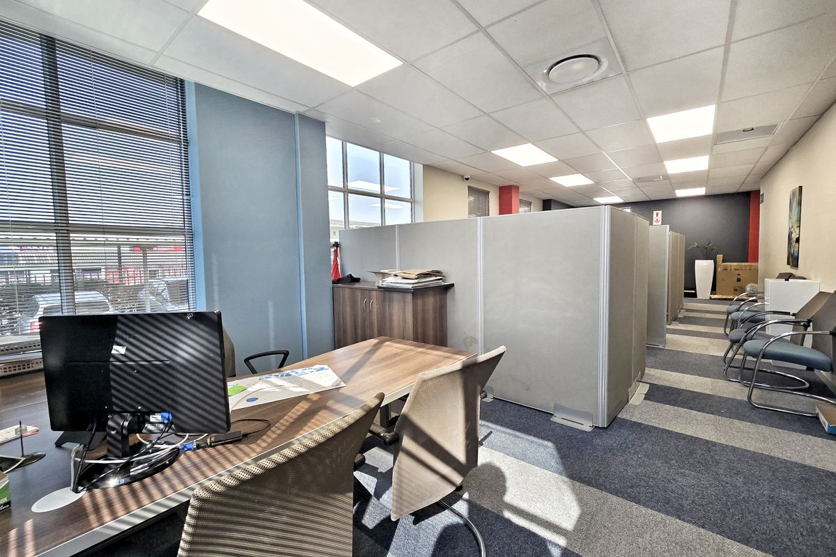Open-plan office space featuring modular partition walls, suspended ceilings with recessed lighting, and large windows with venetian blinds.