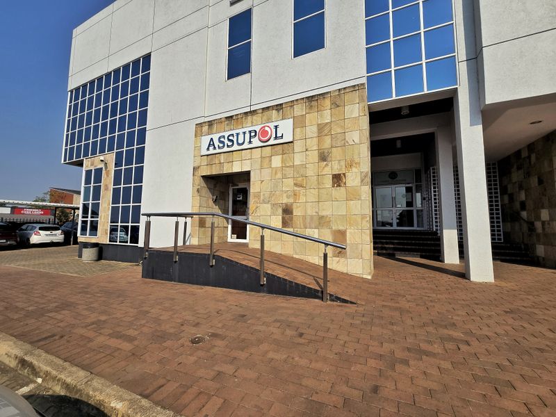 Front facade of a commercial office building featuring stone cladding, a wheelchair-accessible ramp with metal handrails, and large glass windows.