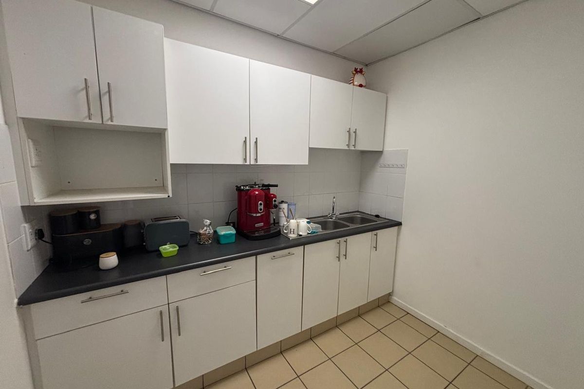 A functional office kitchenette featuring white built-in cabinetry, a dark laminate countertop, a stainless steel sink, and durable tiled flooring.