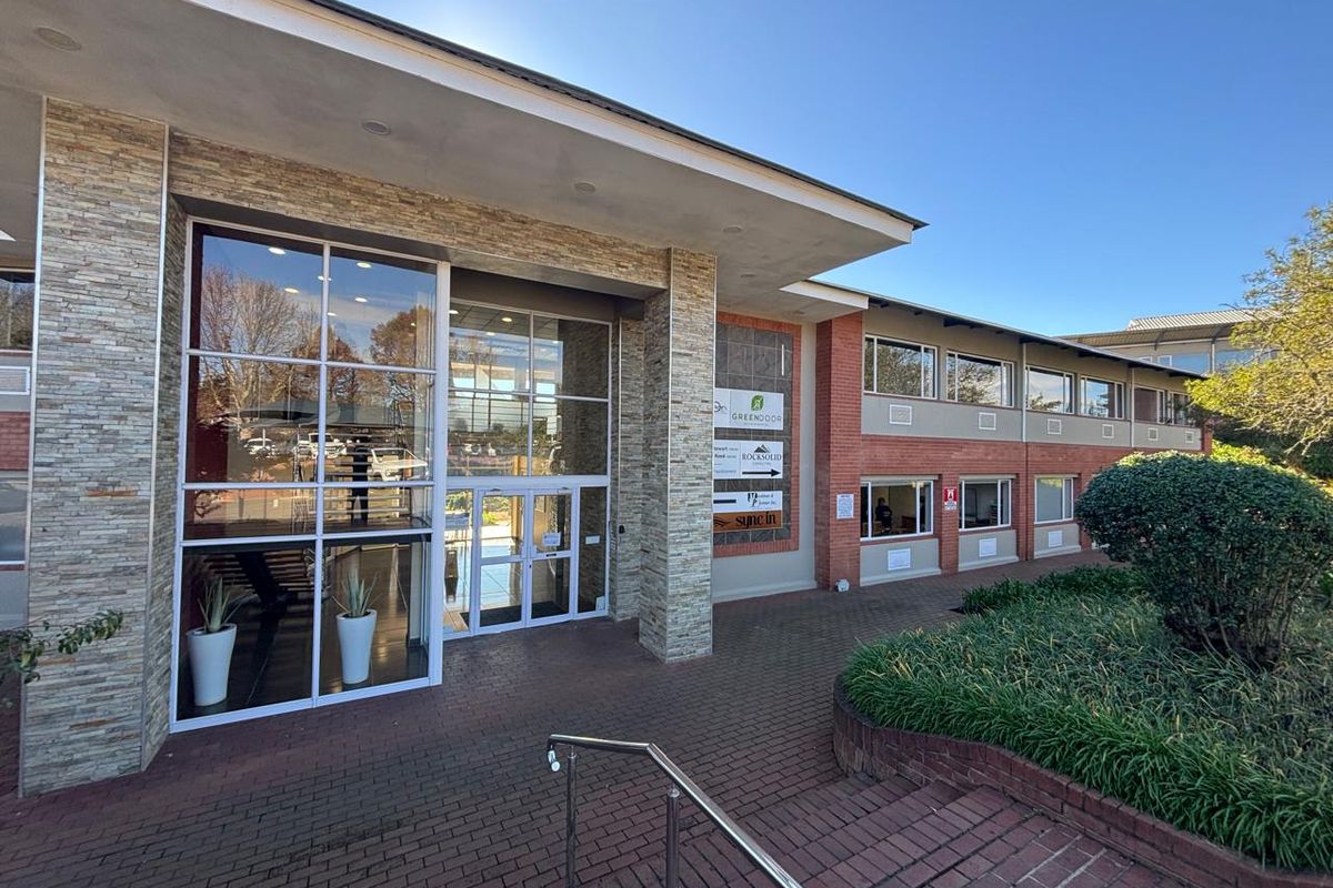 Modern office building entrance featuring stone cladding, extensive glass facade, and brick paved approach with professional landscaping.
