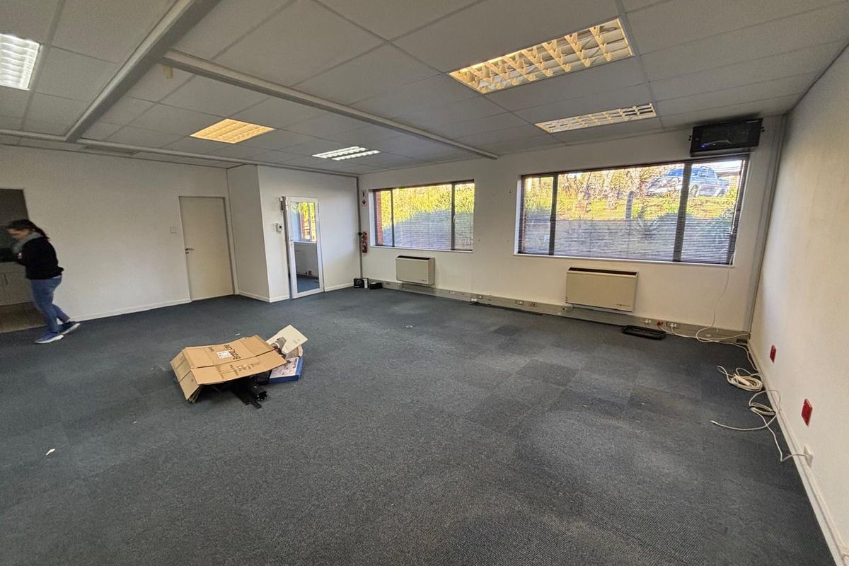Spacious open-plan office area featuring suspended ceilings, recessed lighting, wall-mounted air conditioning units, and carpeted flooring.